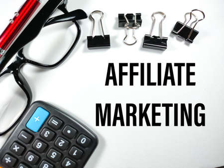 Business concept.Text AFFILIATE MARKETING with pen,glasses,paper clips and calculator on white background.の写真素材
