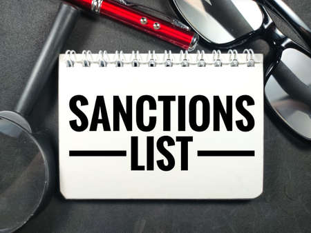 Business concept.Text SANCTIONS LIST with pen,glasses and magnifying glass on black background.の写真素材