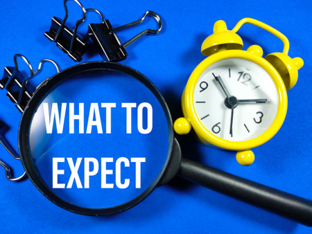 Business concept.Text WHAT TO EXPECT  with magnifying glass,paper clips and clock on blue...