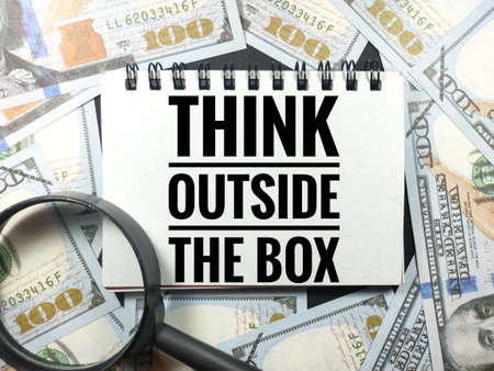 Business concept.Text THINK OUTSIDE THE BOX with magnifying glass and banknote on black background.の写真素材