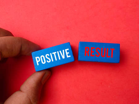 Hand holding colored block with text POSITIVE RESULT on red background.の写真素材