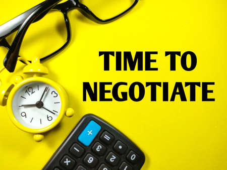 Business concept. Text TIME TO NEGOTIATE with clock,calculator and glasses on yellow backgroundの写真素材