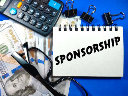 Business concept.Text Sponsorship on notebook with banknote,glasses,calculator and paper clips on blue background.の写真素材