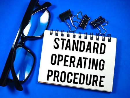 Business concept.Text Standard Operating Procedure on notebook with glasses and paper clips on blue background.の写真素材
