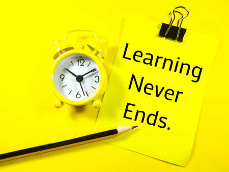 Education concept.Text Learning Never Ends on colorful paper note with pencil and alarm clock on yellow background.の写真素材