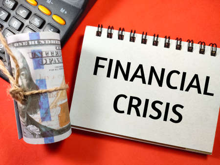 Finance concept.Text FINANCIAL CRISIS with banknote and calculator on red background.の写真素材