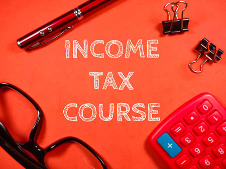 Business concept. Text INCOME TAX COURSE with pen,glasses,paper clips and calculator on red background.の写真素材