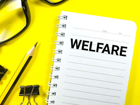 Finance concept.Text WELFARE on notebook with glasses,paper clips and pencil on yellow background.の写真素材