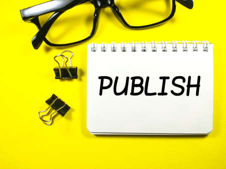 Education concept.Text PUBLISH on notebook with glasses and paper clips on yellow background.の写真素材