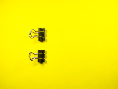 Selective focus.Two paper clips on yellow background with copy and text space.
