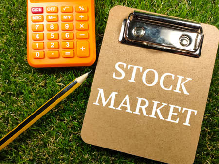 Clipboard with text STOCK MARKET with pencil and calculator on grass background.の写真素材