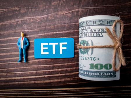 Miniature people with a roll of paper money with the letters or the word ETF on wooden background.の写真素材