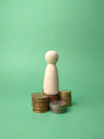 Wooden people figures and coins on a green background.の写真素材