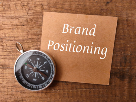 Compass and brown card with text Brand Positioning on a wooden background.