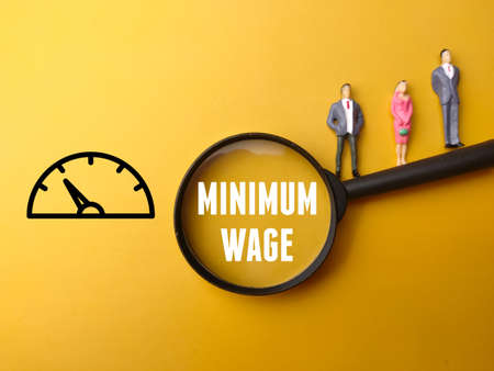 Miniature people, magnifying glass and icon with text MINIMUM WAGE on yellow background.の写真素材