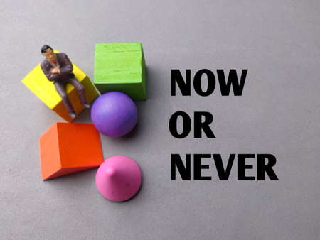 Top view miniature people and colored block with text NOW OR NEVER on gray background.の写真素材