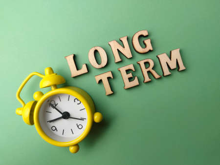 Top view wooden word and clock with word Long Term on green background.の写真素材