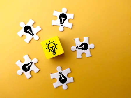 Colored cubes and white puzzle with light bulb icons on lit and dim bulbs.の写真素材