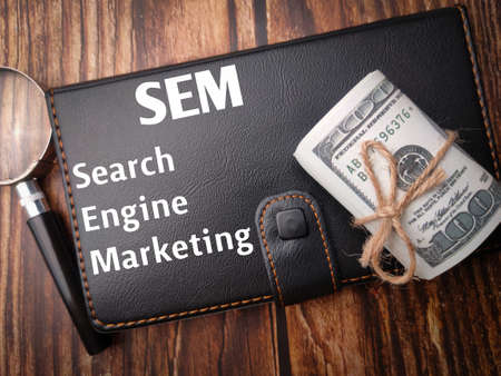 Top view banknotes,magnifying glass and notebook with the word Search Engine Marketing on wooden background.の写真素材