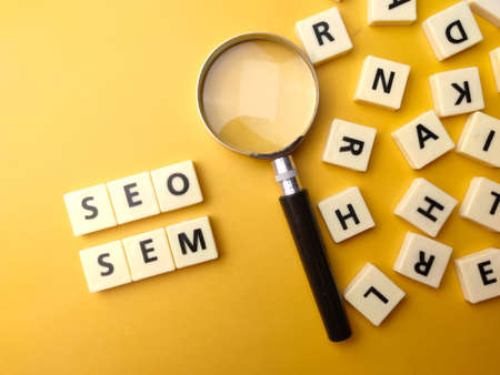 Magnifying glass and toys word with the word SEO and SEM on yellow background. Business concept.の写真素材