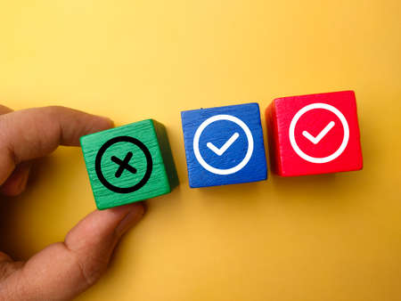 Hand holding colored block with the symbol wrong and correct on yellow background.の写真素材