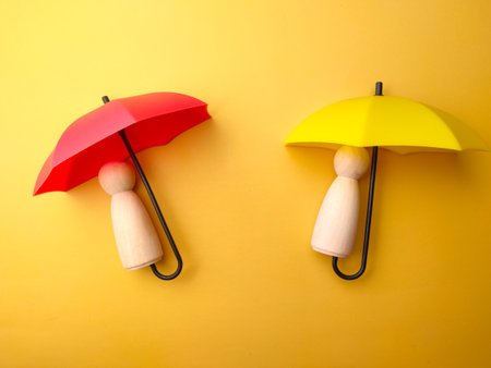 Wooden figures covered by umbrella on a yellow background. Personal insurance concept.の写真素材