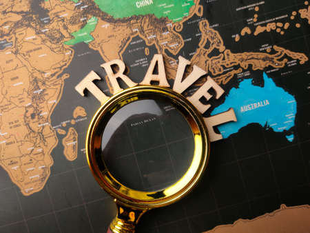 Magnifying glass and wooden word with the word TRAVEL on a world map background.の写真素材