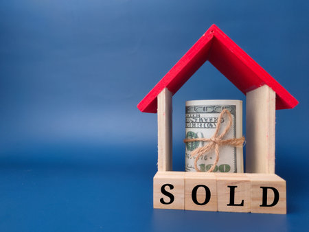 Toy house and banknotes with the word SOLD on a blue background.