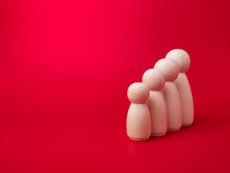 Wooden figures lined up according to their respective heights on red background with copy space.の写真素材