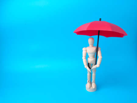 Wooden mannequin holding red umbrella on a blue background with copy space. Insurance and protection concept.の写真素材