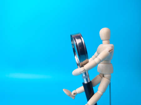 Wooden mannequin holding magnifying glass on a blue background with copy space.の写真素材