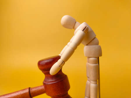 Wooden mannequin holding wooden gavel on a yellow background. Law concept.の写真素材