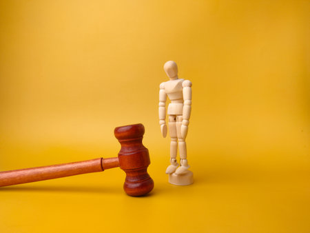 Wooden mannequin and gavel on a yellow background. Law concept.の写真素材