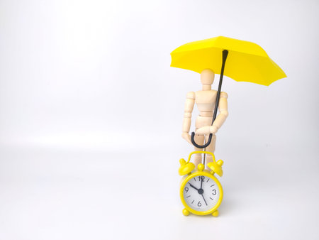 Wooden mannequin holding yellow umbrella and alarm clock on a white background.の写真素材