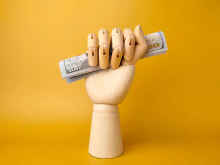 Wooden hand gripping banknotes on a yellow background.の写真素材