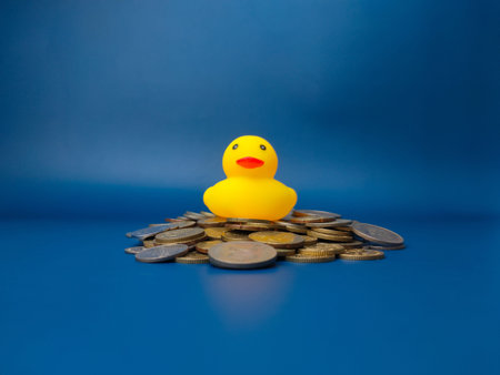 A toy yellow duck is on top of a stack of coins on a blue background. Business concept.