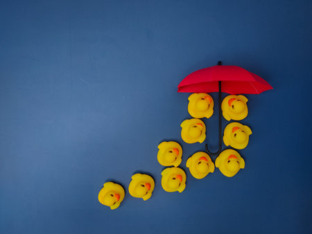 Red umbrellas and yellow ducks on a blue background. The concept of insurance coverage.の写真素材