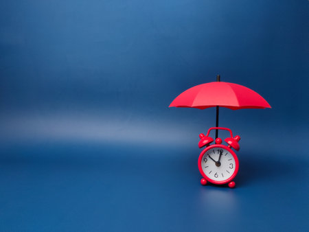 Red umbrella and red clock on a blue background. The concept of insurance coverage..の写真素材