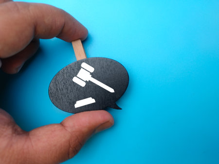 Hand holding wooden board with gavel icon on blue background.の写真素材
