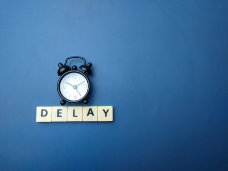Black alarm clock with the word DELAY on blue background with copy space.