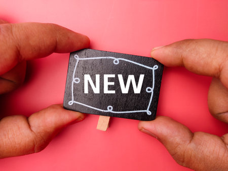 Hand holding wooden board with text NEW on red background.の写真素材