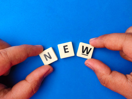 Hand holding toys letters with the word NEW on blue background.の写真素材