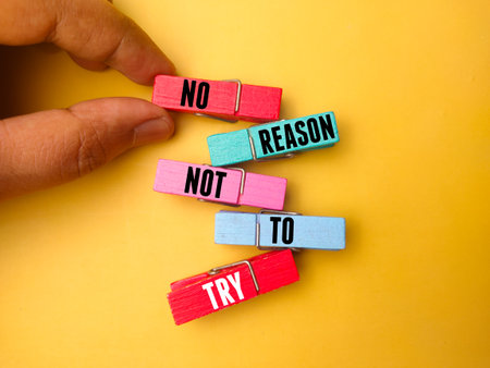Hand holding wooden clips with the word NO REASON NOT TO TRY on yellow background.の写真素材