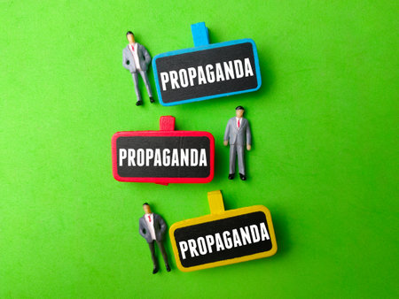 Miniature people and wooden board with the word PROPAGANDA on green background. Business concept.の写真素材