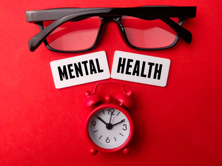 Alarm clock and glasses with the word MENTAL HEALTH on red background.の写真素材