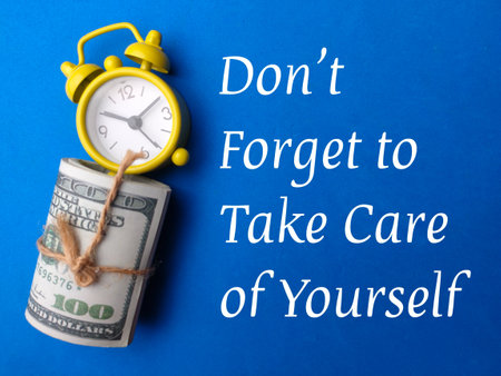 Clock and banknotes with text Dont forget to take care of yourself on a blue background.の写真素材