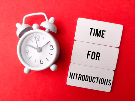 Alarm clock and wooden board with the word TIME FOR INTRODUCTIONS on red background.の写真素材