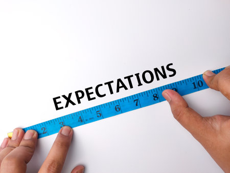 Hand holding blue measuring tape with the word EXPECTATIONS on a white backgroundの写真素材