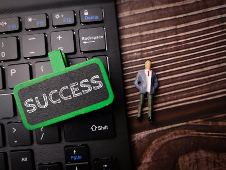 Miniature people and keyboard with the word SUCCESS on a wooden backgroundの写真素材