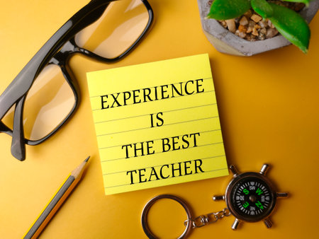 Sticky note and glasses with the word EXPERIENCE IS THE BEST TEACHER on yellow backgroundの写真素材